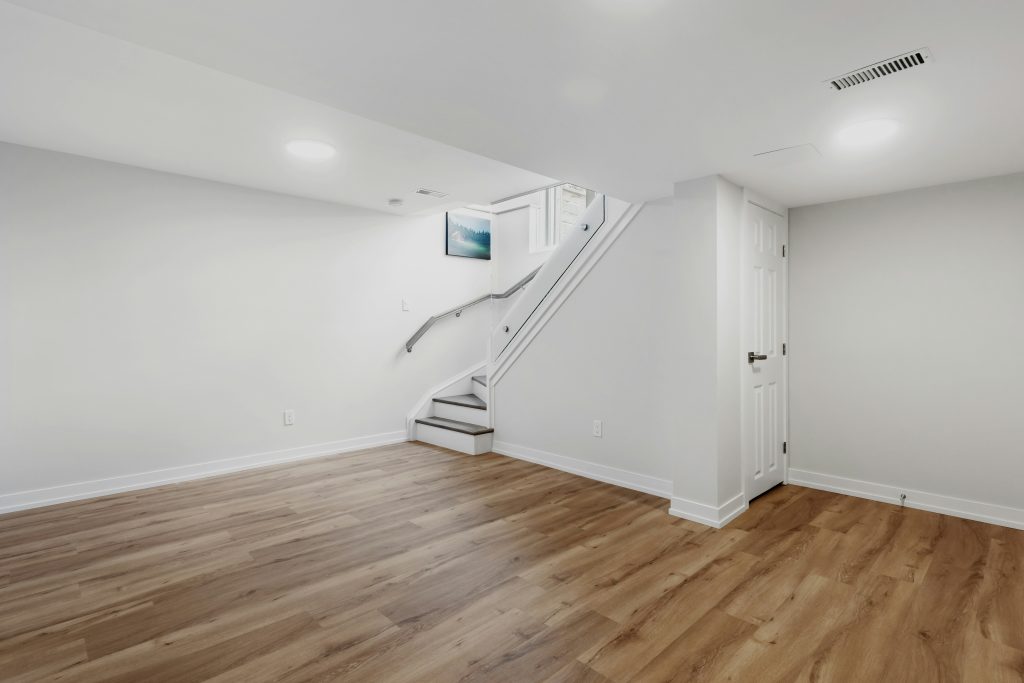 Finished basement remodeling featuring luxury vinyl flooring, custom storage cabinets, built-in workspace, recessed lighting, and modern staircase in Cary, NC.