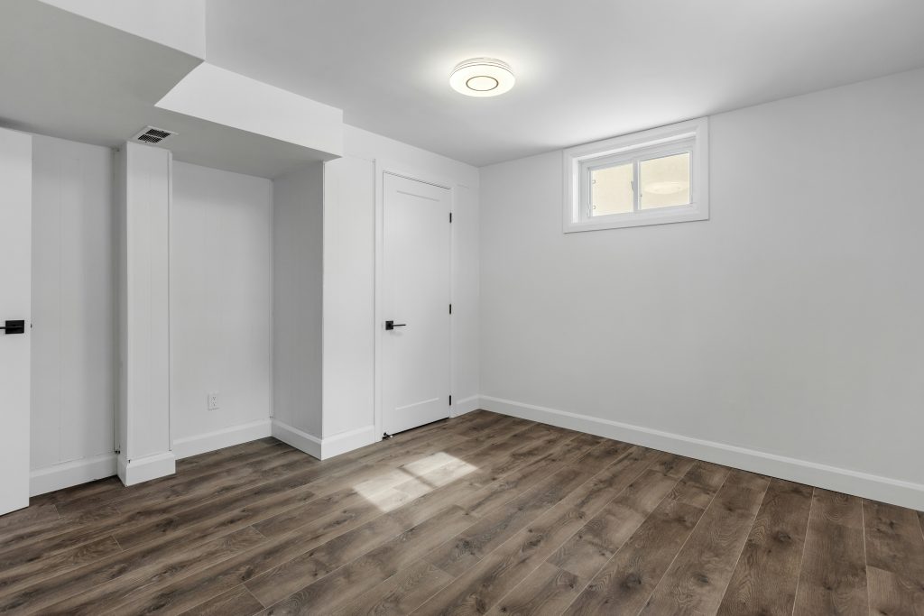 Finished basement room featuring luxury vinyl flooring, modern white walls, recessed lighting, natural daylight window, and contemporary finishes in Cary, NC.